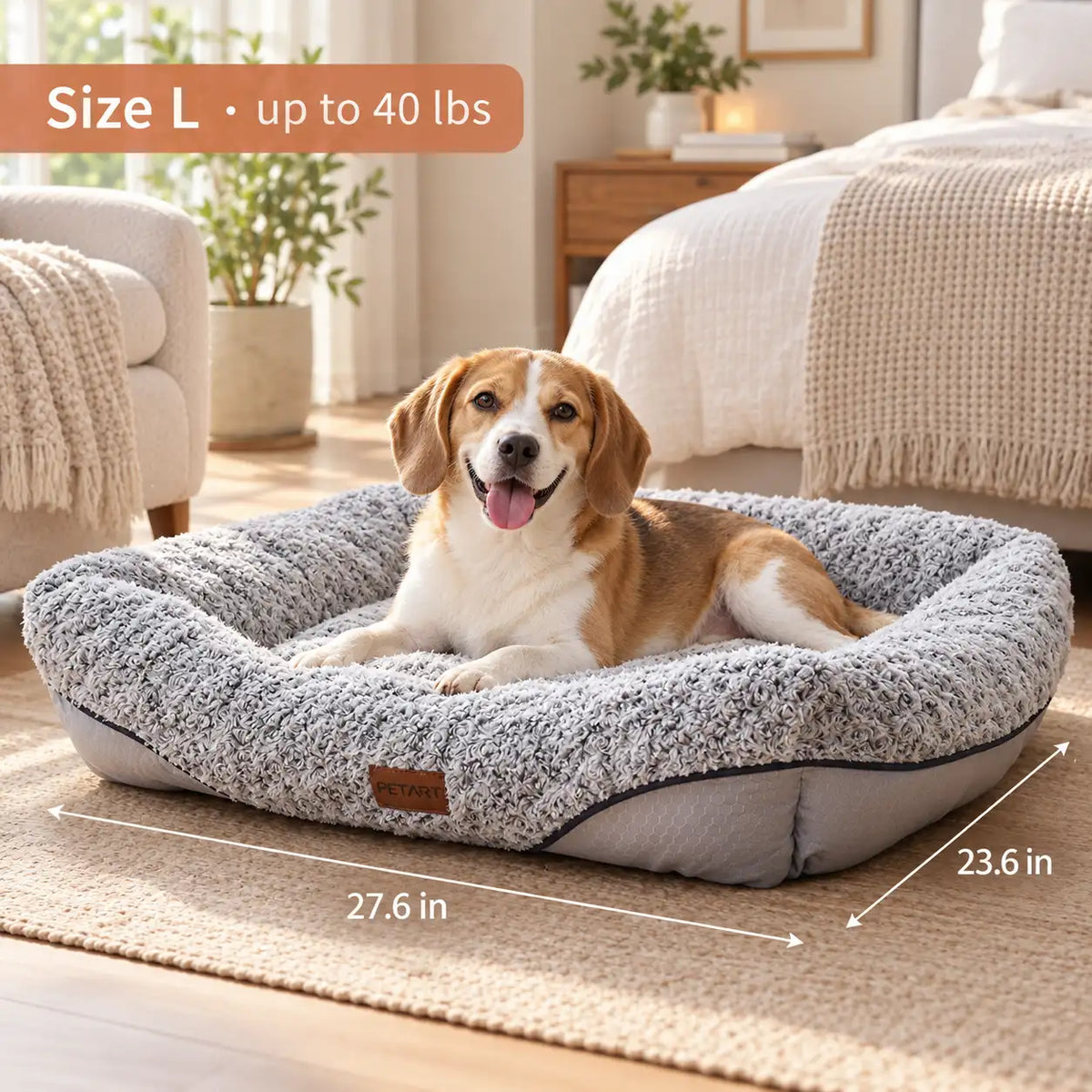 A tan and white dog lies in a large gray textured pet bed on a beige rug in a bright bedroom. White dimension arrows and text show the bed is Size L, with measurements 27.